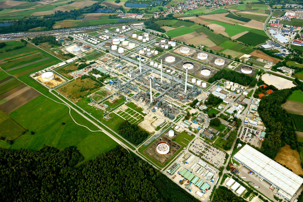 Luftaufnahme der Bayernoil Raffinerie mit markanter Struktur aus Lagertanks, Rohrleitungen und Produktionsanlagen in grüner Umgebung.